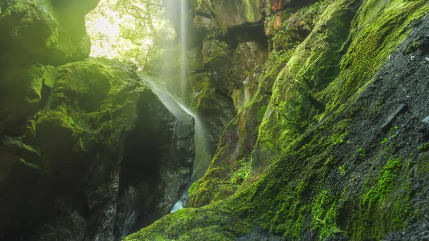 Thin waterfall flows through gap between moss covered mountains