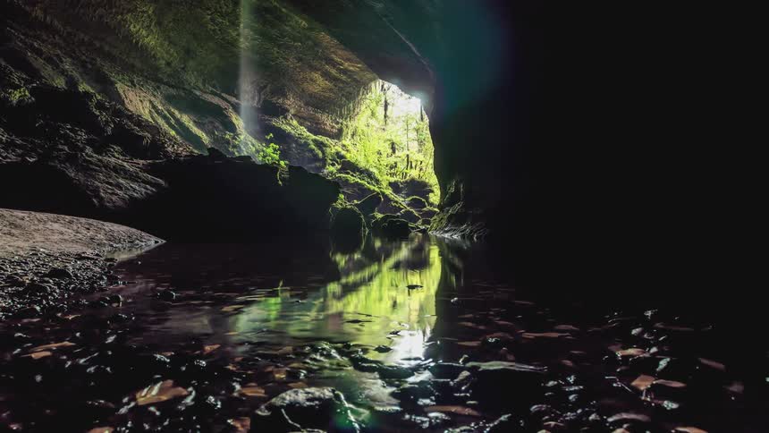 Stream flows away from cave mouth and deeper into cavern on a summer day