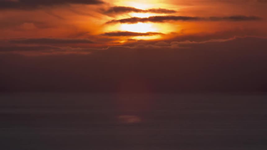 Time lapse of a sunset over the ocean behind a thick layer of clouds