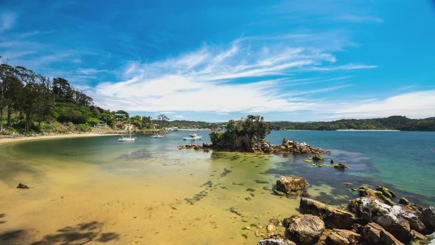 Serene natural landscape with a lake of calm waters surrounded by vegetation and rocks under a blue sky with scattered clouds