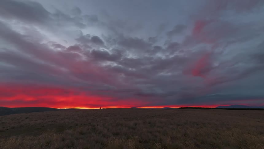 Dark clouds flow and twist over a large grassy plain
