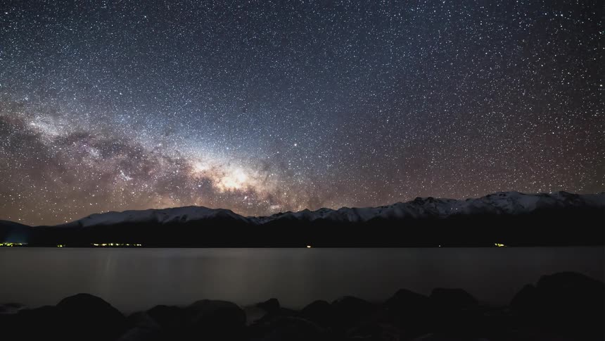 Time lapse of a starry night sky over a lake and mountains