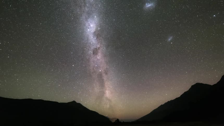 Starry night sky rotates above silhouetted mountains