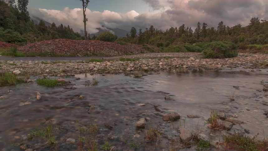 Dark storm clouds move over a forest and stream