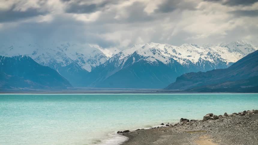 Crystal clear lake surrounded by snowy mountains and misty clouds passing by
