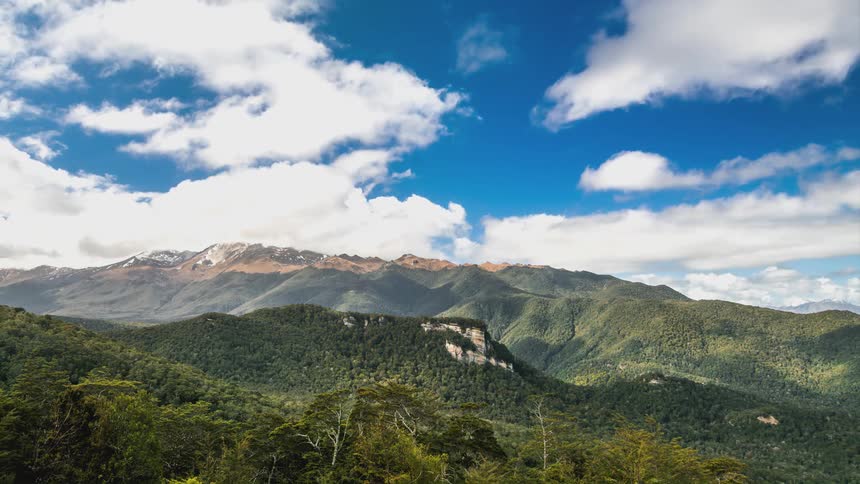 White clouds cast shadows on a large forested mountain range