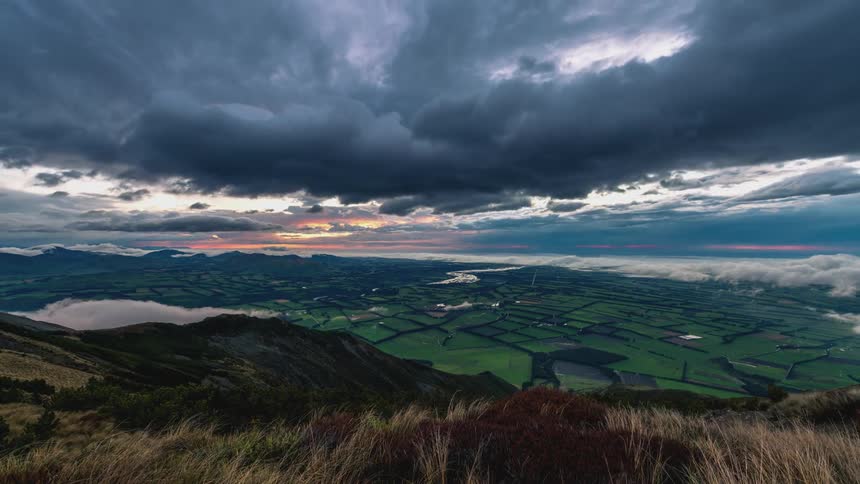 Time lapse of clouds rolling over a rural landscape of green fields at evening