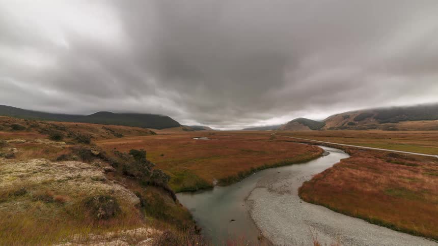 Vast landscape with a winding river surrounded by grassy fields and hills under a cloudy sky