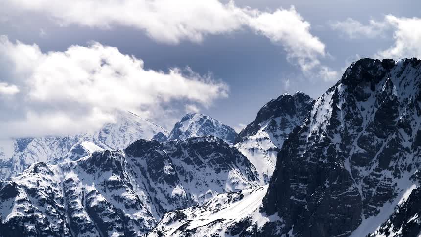 Clouds flow over a range of steep snow dusted mountains