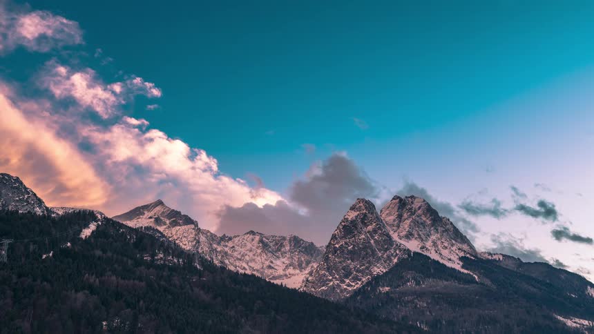 Landscape of snowcapped mountains under a dramatic sky with dense clouds and illuminated by the setting sun