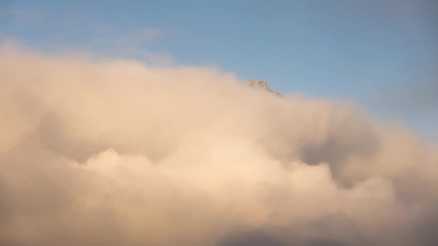Thick and dense clouds cover all but the peak of a mountain