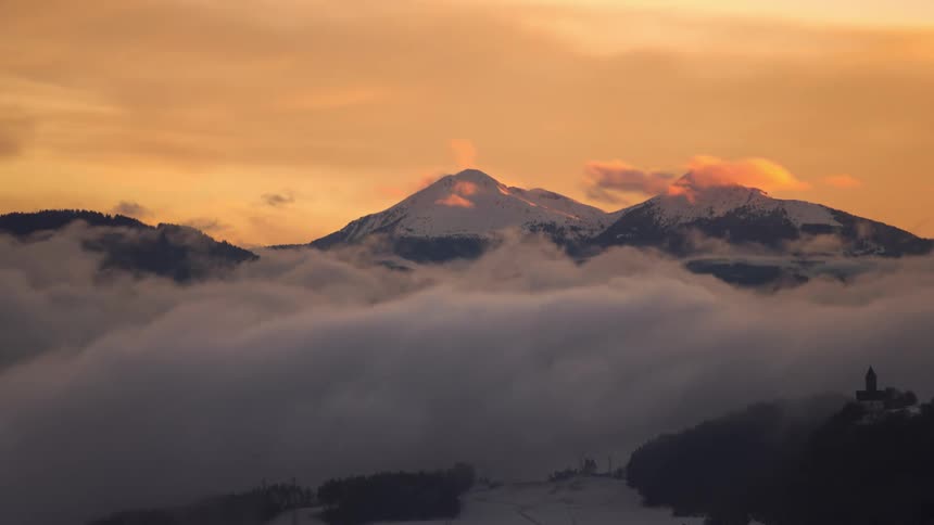 Mountains with snowcapped peaks in a sea of clouds with the sky turning red
