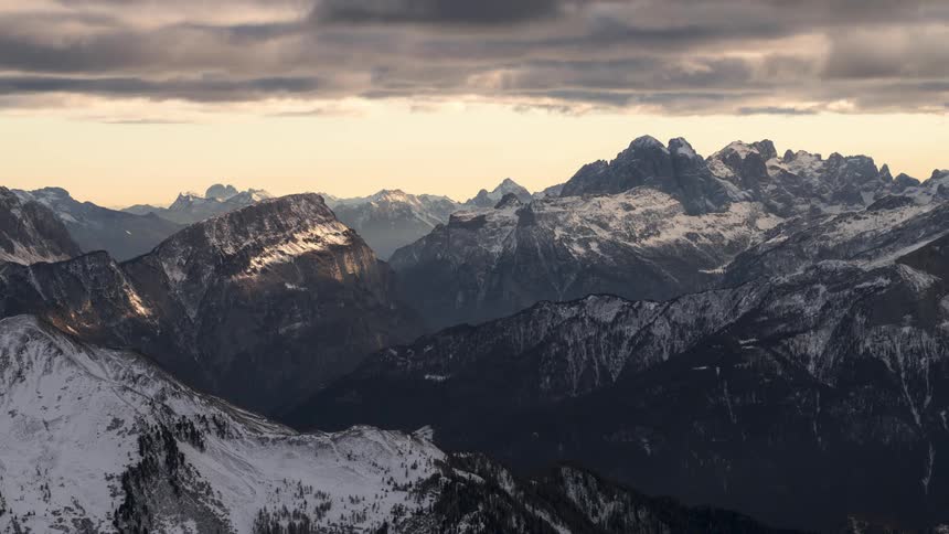 A mountain range with its snowcovered peaks and there are clouds moving quickly in the sky