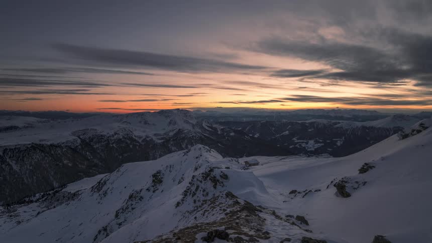 A mountain range of snow covered mountains illuminated by sunlight and then darkens several dark clouds are in the sky
