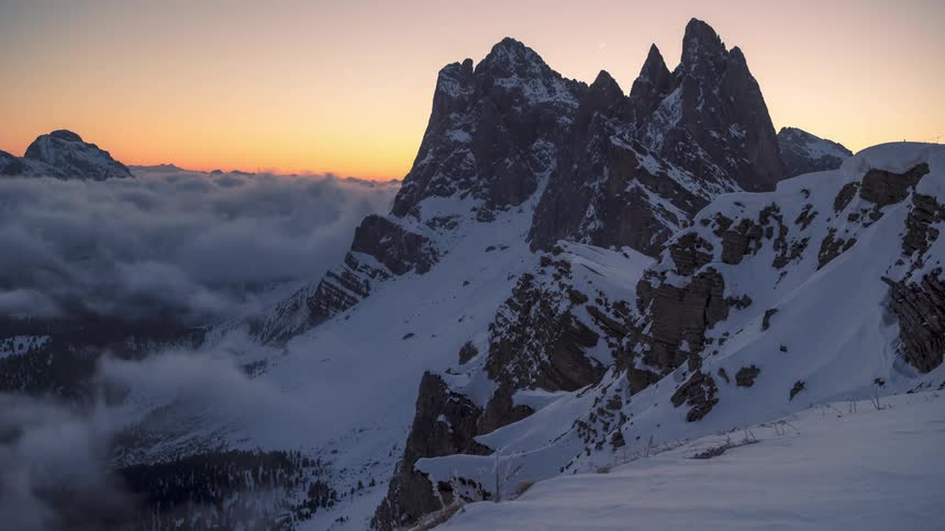Sea of clouds next to mountains with orange sky