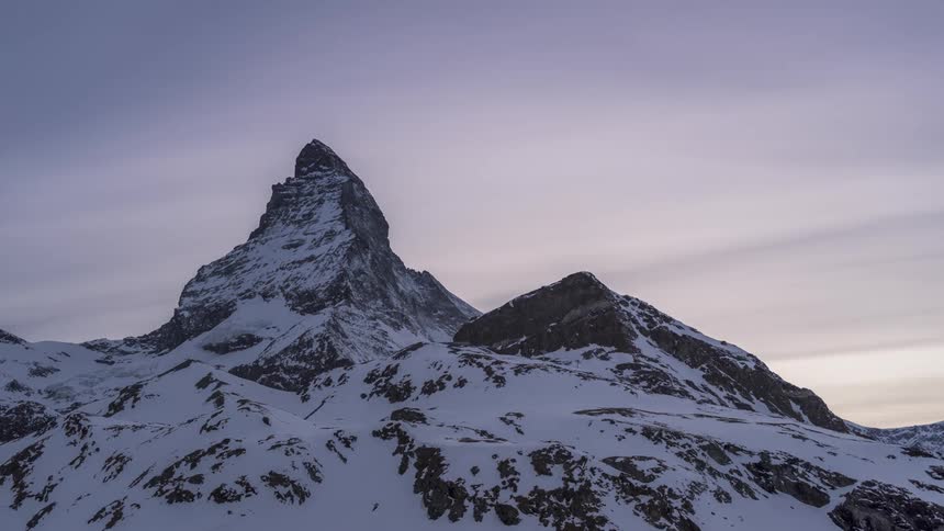 Time lapse of high clouds rolling over snowcovered mountain peaks from day to night