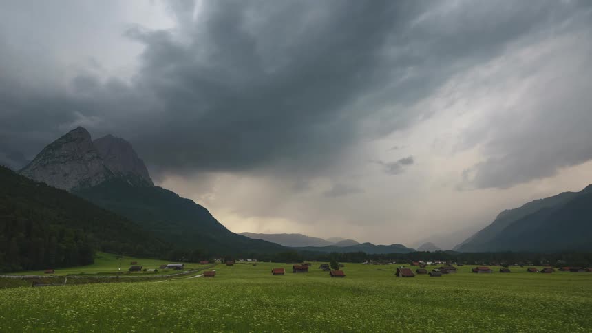Dark storm clouds move over a mountain valley containing a rural community