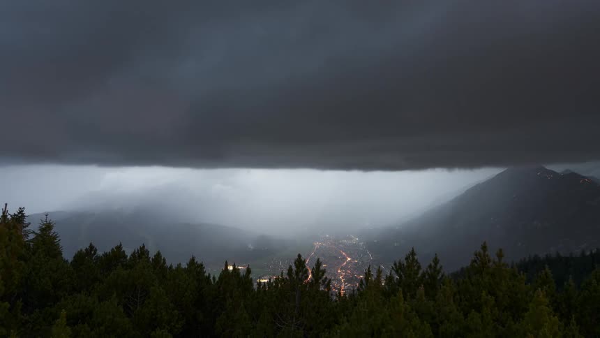 Time lapse of a city nestled in a valley between mountains under rolling storm clouds