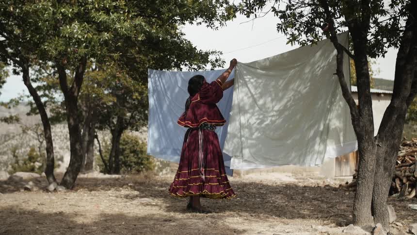 A woman in native dress hangs sheets on a clothesline