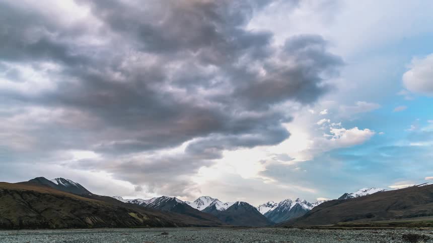 Natural landscape with mountains partially covered in snow in the background and a dramatic sky with dense clouds