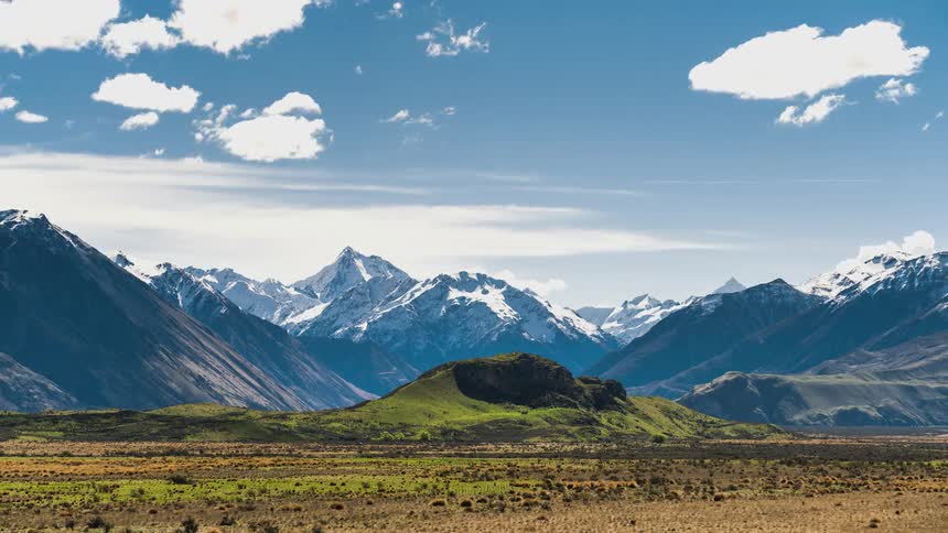Fluffy white clouds pass over a vast mountain range and plain