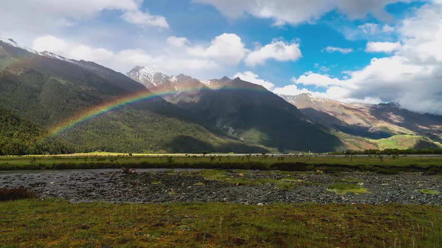 Time lapse of clouds rolling over a mountainous landscape with a rainbow in front