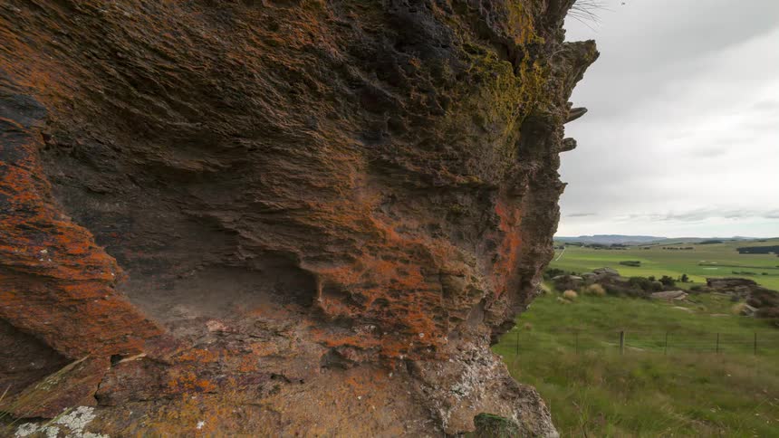 Dark clouds move over fields and a curious rock formation