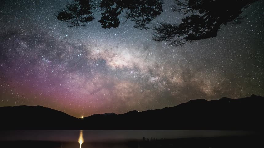 Starry sky with the silhouette of mountains on the edge of a lake