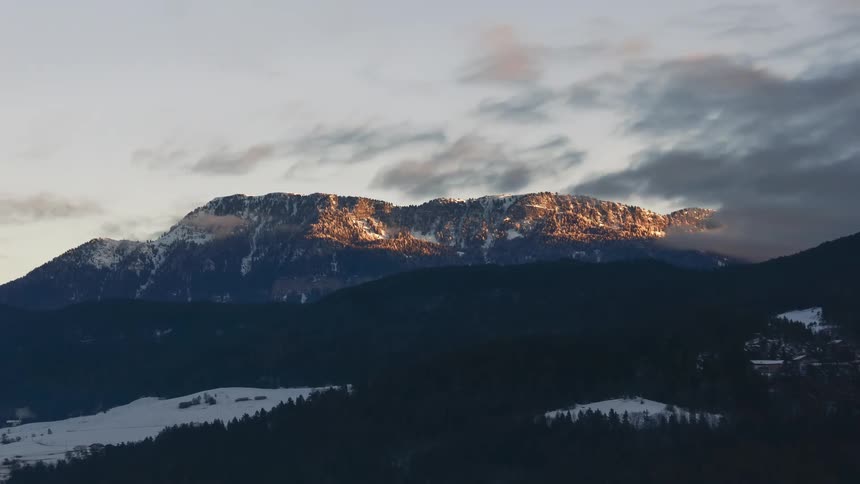 Dark clouds gather over mountain towering over forest during winter