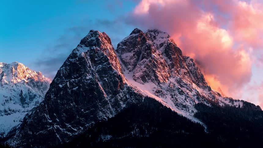 Clouds move over a snowcovered mountain peak at sunset