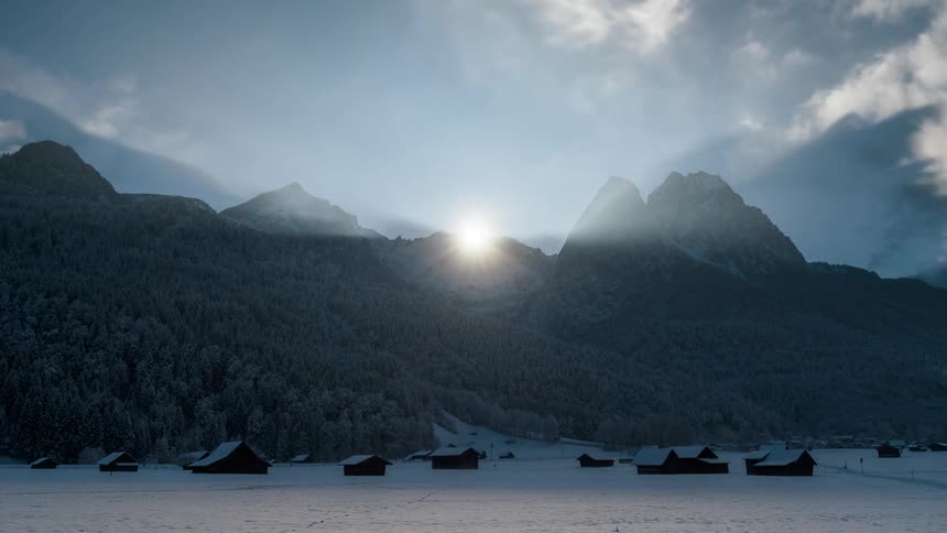 Sun rising behind mountains and houses on a snowcovered ground