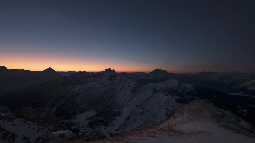 The sun sets and lights flash on the mountains