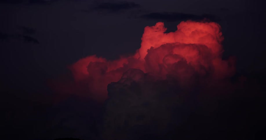 Cloud illuminated in vibrant tones at sunset with the day getting dark