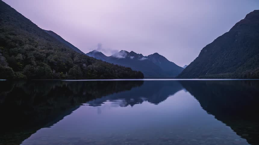 Lake surrounded by mountains with clouds passing by and the day dawning