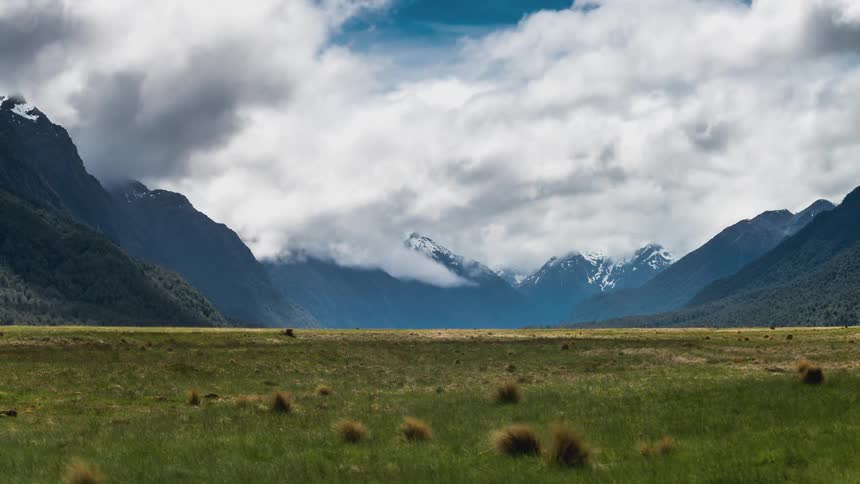 Time lapse of clouds rolling over a vast grassy plain and a distant mountain range