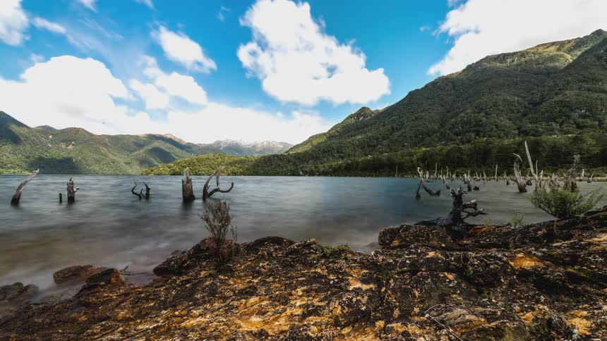 The clouds reflect off the lake by the green hills