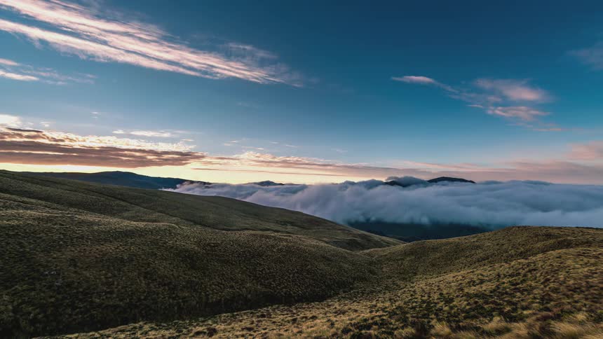 Thick clouds flow over small hills and through a mountain valley