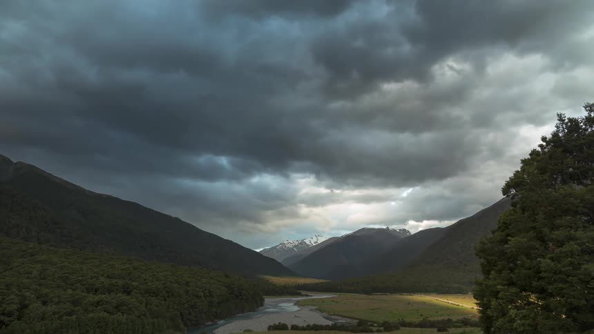 Dark storm clouds pass over a stream flowing through a mountain valley