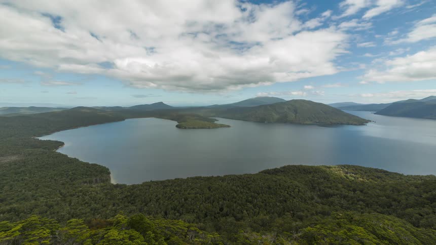 White clouds move over a big lake surrounded by mountains and forests