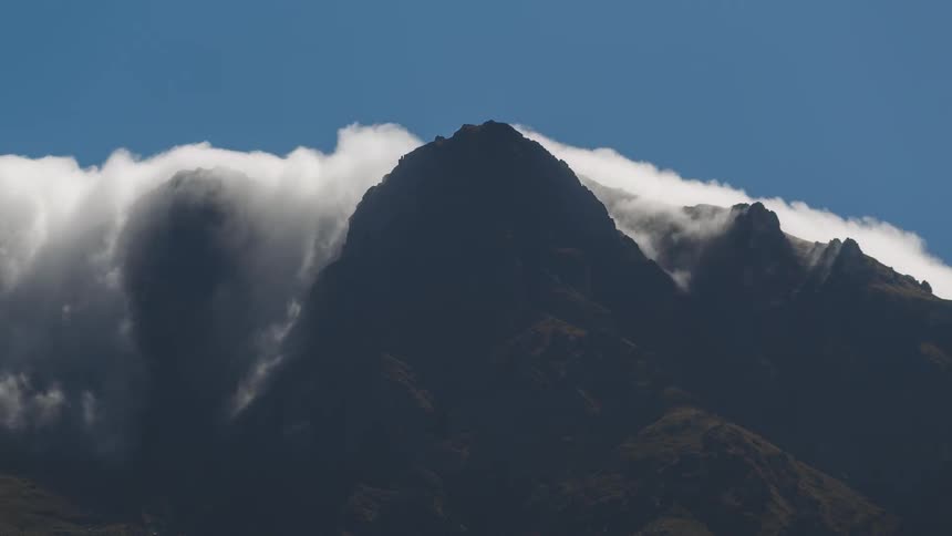 Time lapse of white mountains rolling over mountain peaks under a blue sky