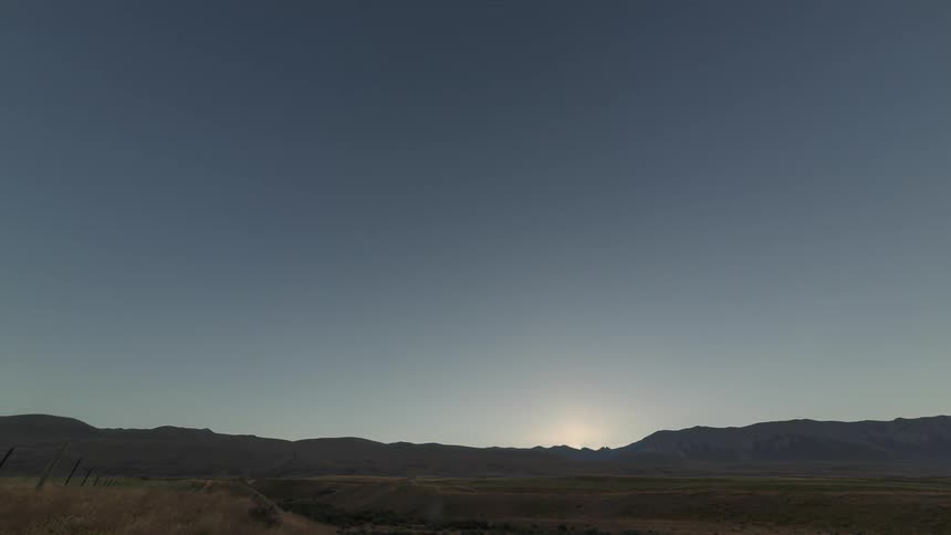 A desert region with the sun coming out from behind mountains in the background in the morning