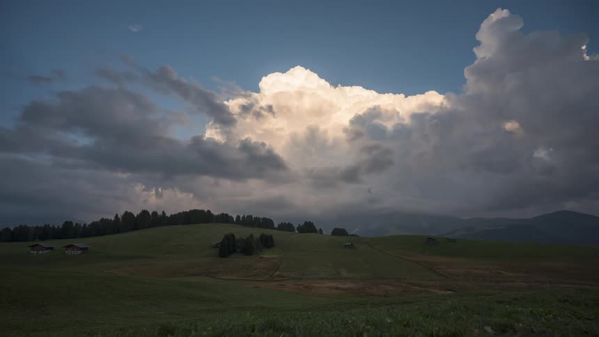 Landscape of a greenish field with the silhouette of mountains on the horizon and the day getting dark with clouds passing by