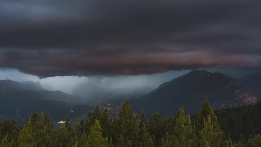 Landscape of mountain ranges and forests against a sky with black clouds