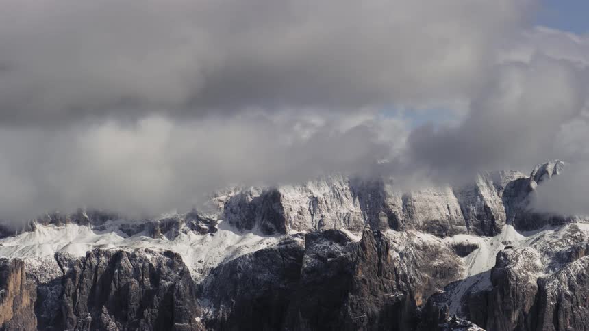 Low lying clouds swirl around snow dusted mountains