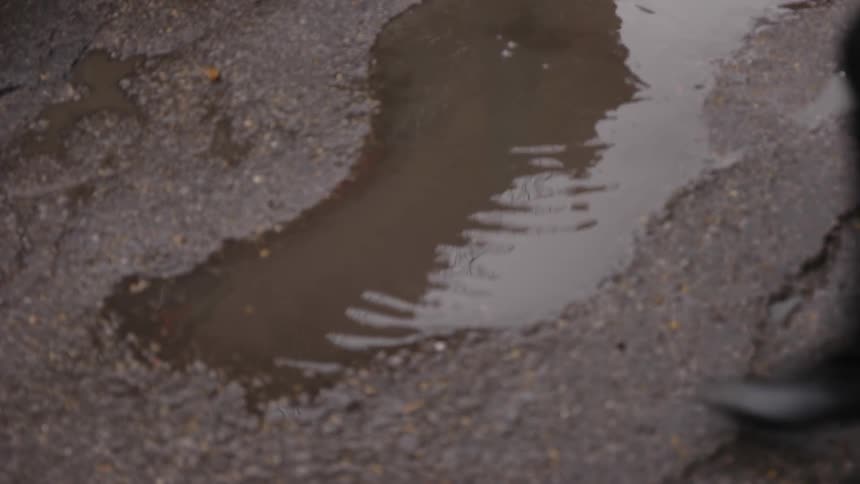 A man stepping in a puddle after two women have stepped over it