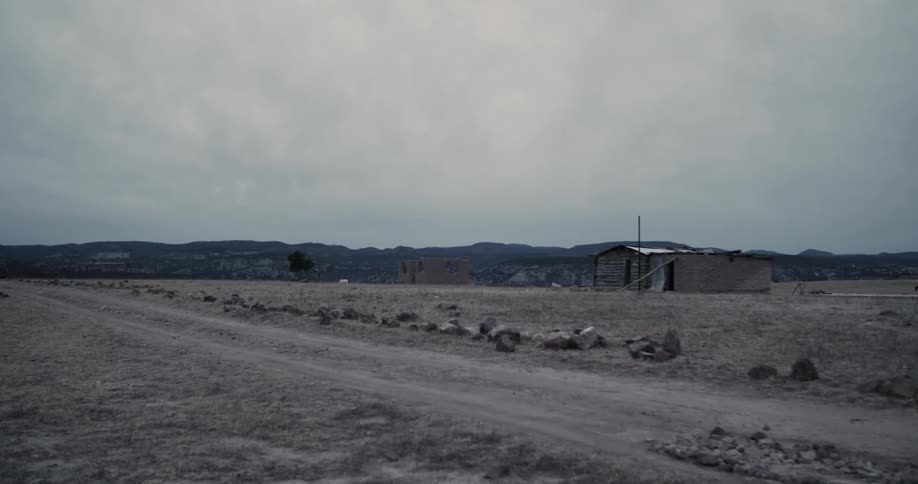 A rundown building sits in a barren field near a dirt road