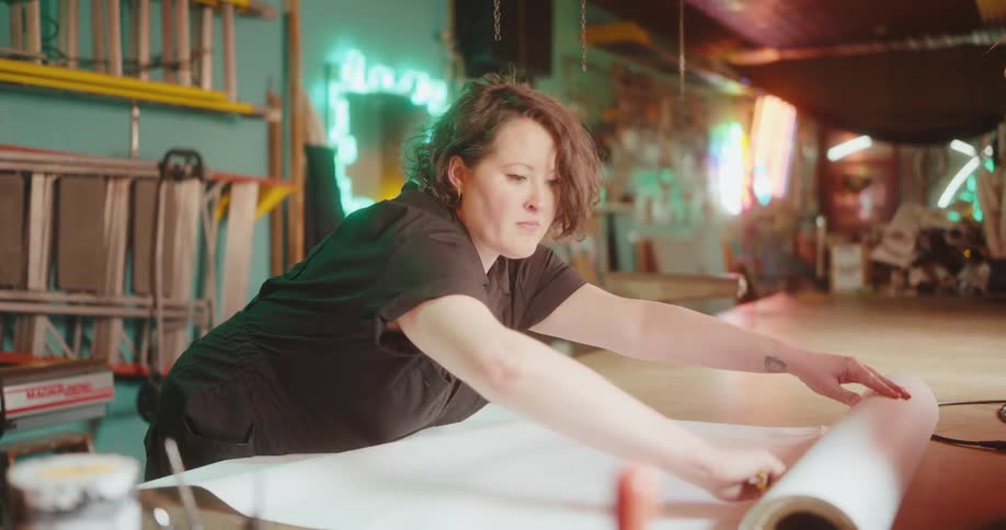 A woman stretches paper from a roll on a work bench and cuts off a part of it