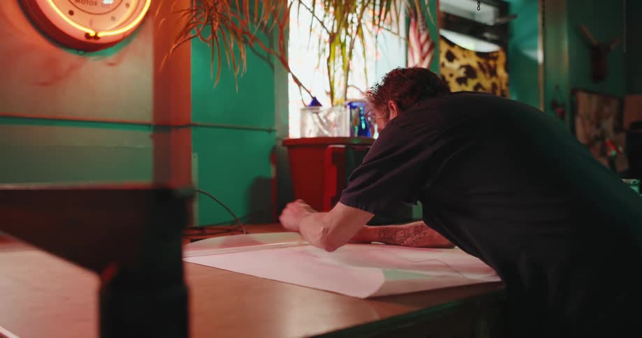Man working and drawing on a large white paper in an environment lit with neon lights