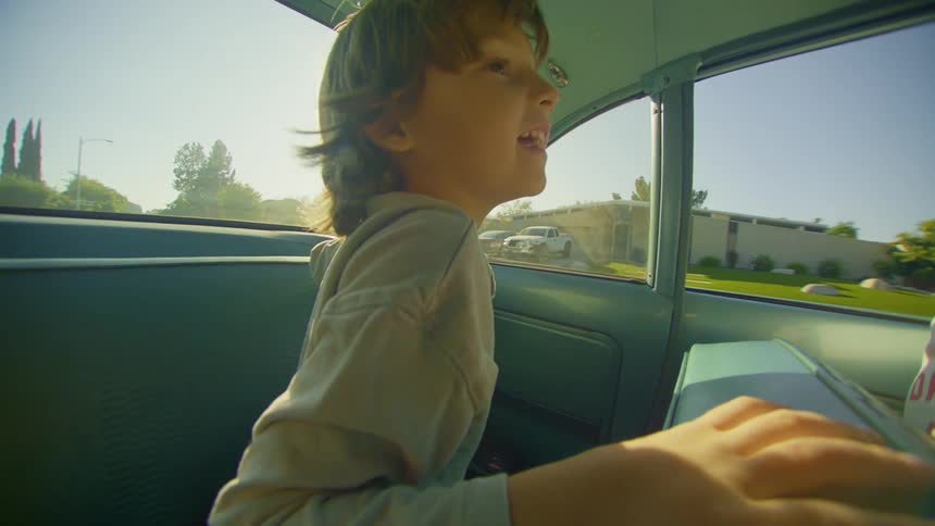 Inside a moving car a young boy looks around with excitement as it drives down the street
