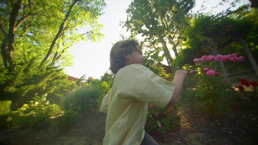 A young boy laughing as he runs across a garden park
